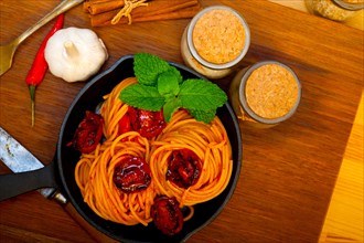 Italian spaghetti pasta and tomato with mint leaves on iron skillet over wood board