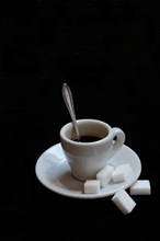 A cup of coffee with sugar cubes on a black background