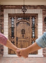 A couple holding his hands approaching the front door of a house