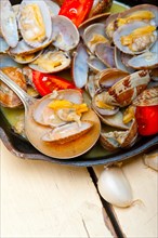 Fresh clams stewed on an iron skillet over wite rustic wood table