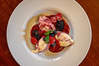 Dumplings made from curd cheese garnished with fresh raspberries and blackberries on a wooden table