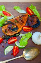 Wood fired hoven cooked chicken breast on wood board with herbs spices and vegetables