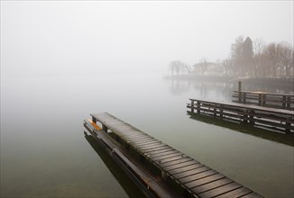 Abandoned bathing jetty in the morning mist on the lake promenade
