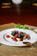 A slice of cheesecake with fresh raspberries and blackberries and a layer of icing sugar on a white plate