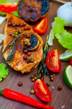 Wood fired hoven cooked chicken breast on wood board with herbs spices and vegetables