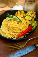 Italian spaghetti pasta with zucchini sauce on iron skillet over wood board