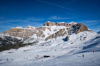 View of a ski resort piste with people skiing in Dolomites in Italy. Ski area Belvedere. Canazei