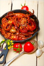 Fresh seafood stew prepared on an iron skillet ove white rustic wood table
