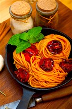 Italian spaghetti pasta and tomato with mint leaves on iron skillet over wood board