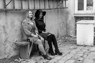 Black and white shot of two female friends on a bench in a backyard. One of the young woman has fair skin and long blonde hair