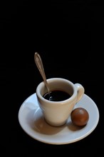 A cup of coffee and chocolate praline on a black background