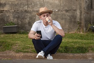 Young man sitting on sidewalk checking phone