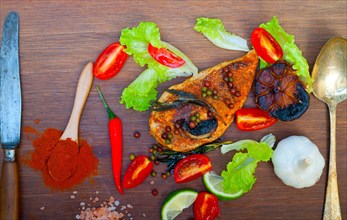 Wood fired hoven cooked chicken breast on wood board with herbs spices and vegetables