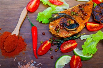 Wood fired hoven cooked chicken breast on wood board with herbs spices and vegetables