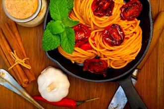 Italian spaghetti pasta and tomato with mint leaves on iron skillet over wood board