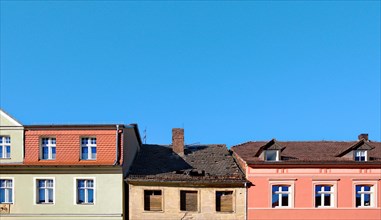 Two renovated and one dilapidated building against a blue sky