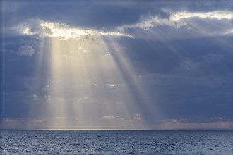 Sun breaks through the clouds with sunrays over sea