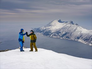 Two ski mountaineers congratulate each other at the summit of Flobjoern overlooking the Bergsfjord