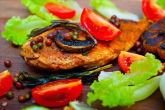 Wood fired hoven cooked chicken breast on wood board with herbs spices and vegetables