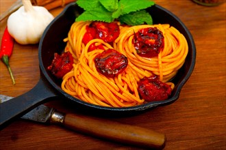 Italian spaghetti pasta and tomato with mint leaves on iron skillet over wood board