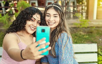 Two pretty girls sitting on a bench taking a selfie