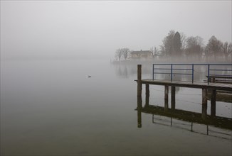 Abandoned bathing jetty in the morning mist on the lake promenade