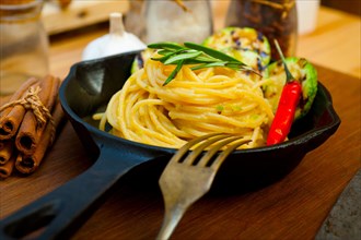 Italian spaghetti pasta with zucchini sauce on iron skillet over wood board