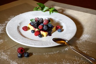 A slice of cheesecake with fresh raspberries and blackberries and a layer of icing sugar on a white plate