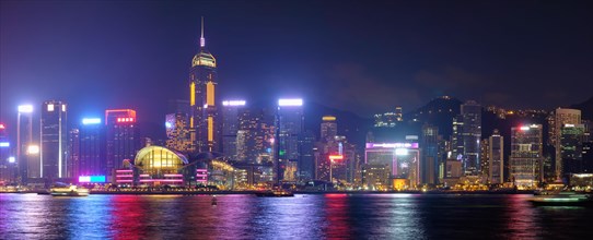 Panorama of Hong Kong skyline cityscape downtown skyscrapers over Victoria Harbour in the evening illuminated tourist boats and ferries