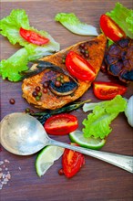 Wood fired hoven cooked chicken breast on wood board with herbs spices and vegetables