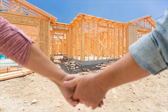 A couple hold his hands and looking at their new house under construction