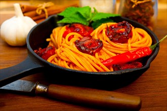 Italian spaghetti pasta and tomato with mint leaves on iron skillet over wood board