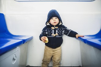 Cute toddler in the hood eating apple on the ferry in winter time
