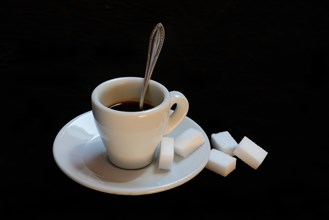 A cup of coffee with sugar cubes on a black background