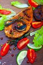 Wood fired hoven cooked chicken breast on wood board with herbs spices and vegetables