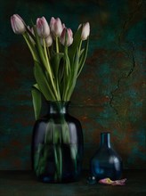 Still life with tulips in glass vase next to empty glass vase and glass ball