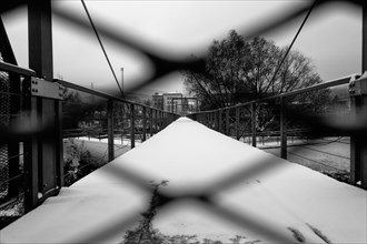 Black-and-white photograph of a path covered with snow and protected from unauthorised access by a grille