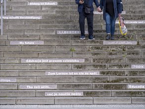 A couple walking down stairs with slogans about education and learning in several languages