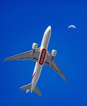 Ein Flugzeug Boeing 777-F1H der Fluggesellschaft Emirates beim Landeanflug auf den Frankfurter Flughafen vor dem Mond