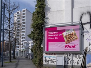Large advertising poster for the delivery service Flink on a house wall in front of a high-rise building