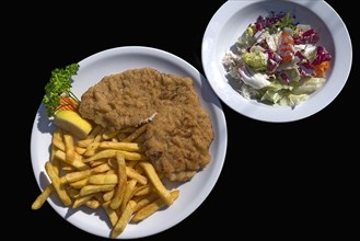 Wiener Schnitzel with french fries and salad on a black background