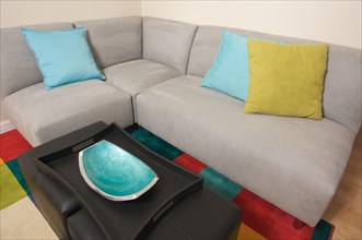 Grey suede couch corner area with colorful rug and pillows