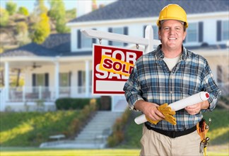 Contractor with plans and hard hat in front of sold for sale real estate sign and house