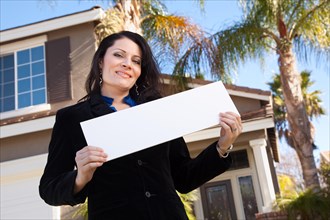 Happy attractive hispanic woman holding blank sign in front of house