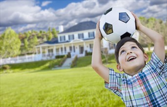 Cute smiling young boy holding soccer ball in front of beautiful house