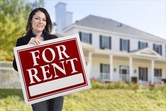 Smiling hispanic female holding for rent sign in front of beautiful house