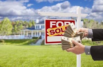 Man handing over thousands of dollars in front of house and sold for sale real estate sign