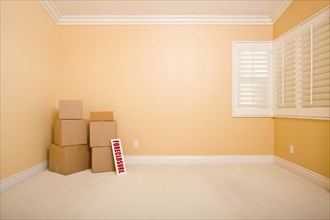 Moving boxes and foreclosure real estate sign on floor in empty room with copy space on blank wall