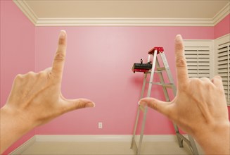 Hands framing pink painted room wall interior with ladder
