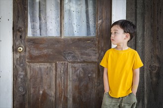 Melancholy mixed-race boy standing in front of door on porch
